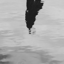 Imatge en blanc i negre d'una superficie aquàtica on s'intueix el reflex d'una persona.